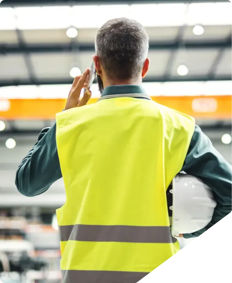 Man in a yellow hi-vis vest with his helmet under his arm, talking on the phone.