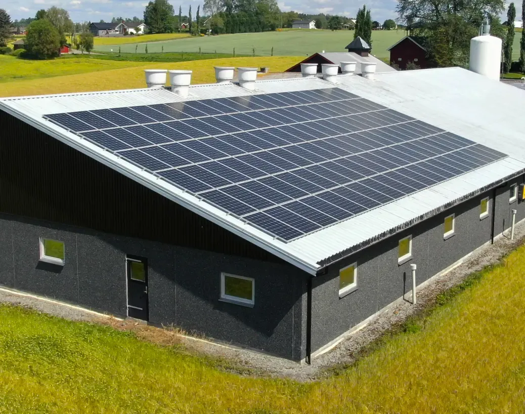 Farm building with solar panels across the whole roof, surrounded by green fields.