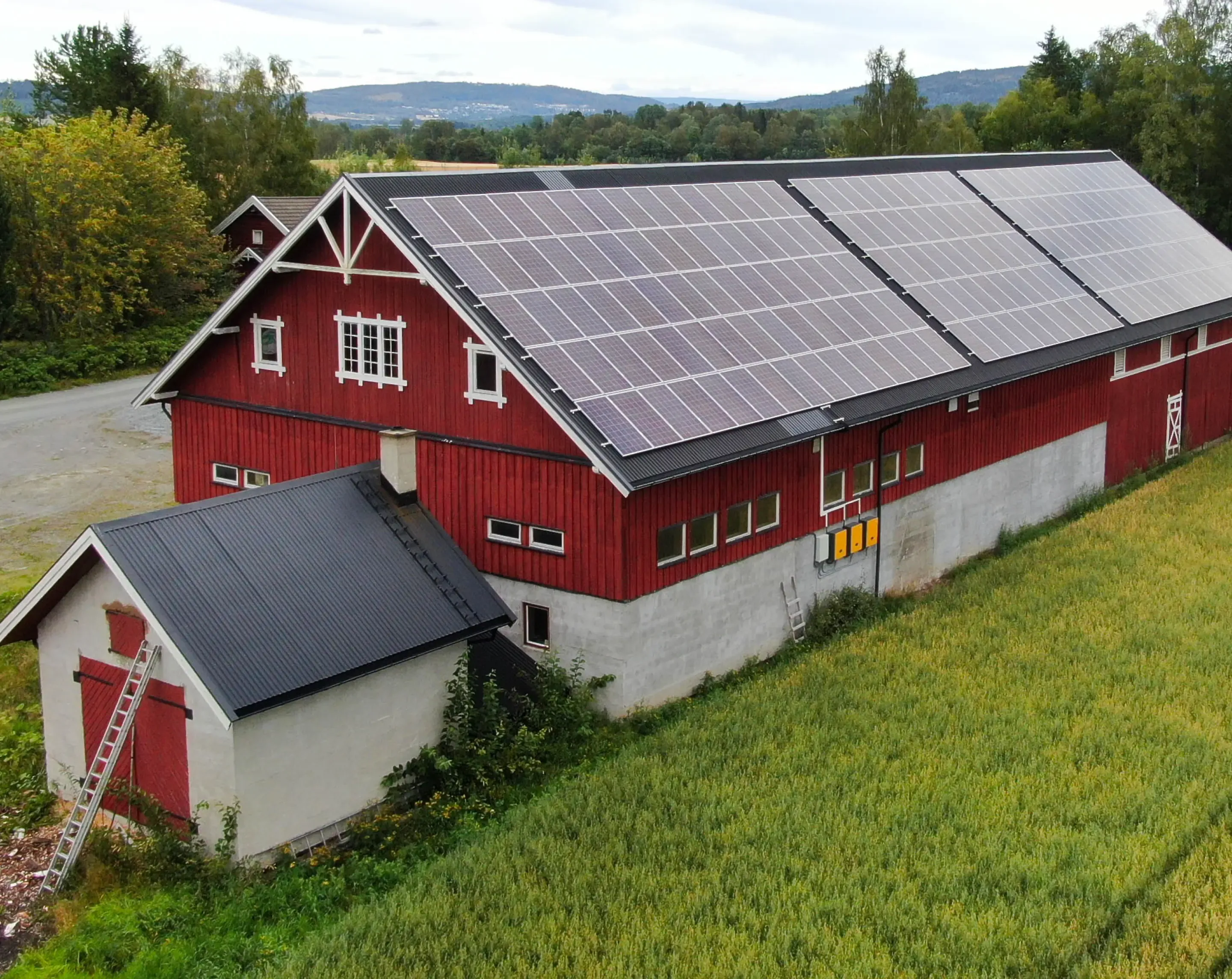 Large red barn with solar panels across one whole roof surface, with fields and wooded hills behind.