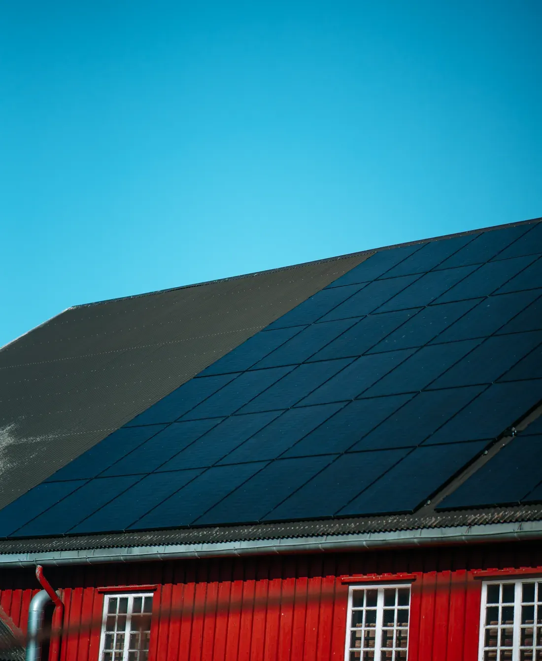 Sorte solcellepaneler på taket til en rød låve.