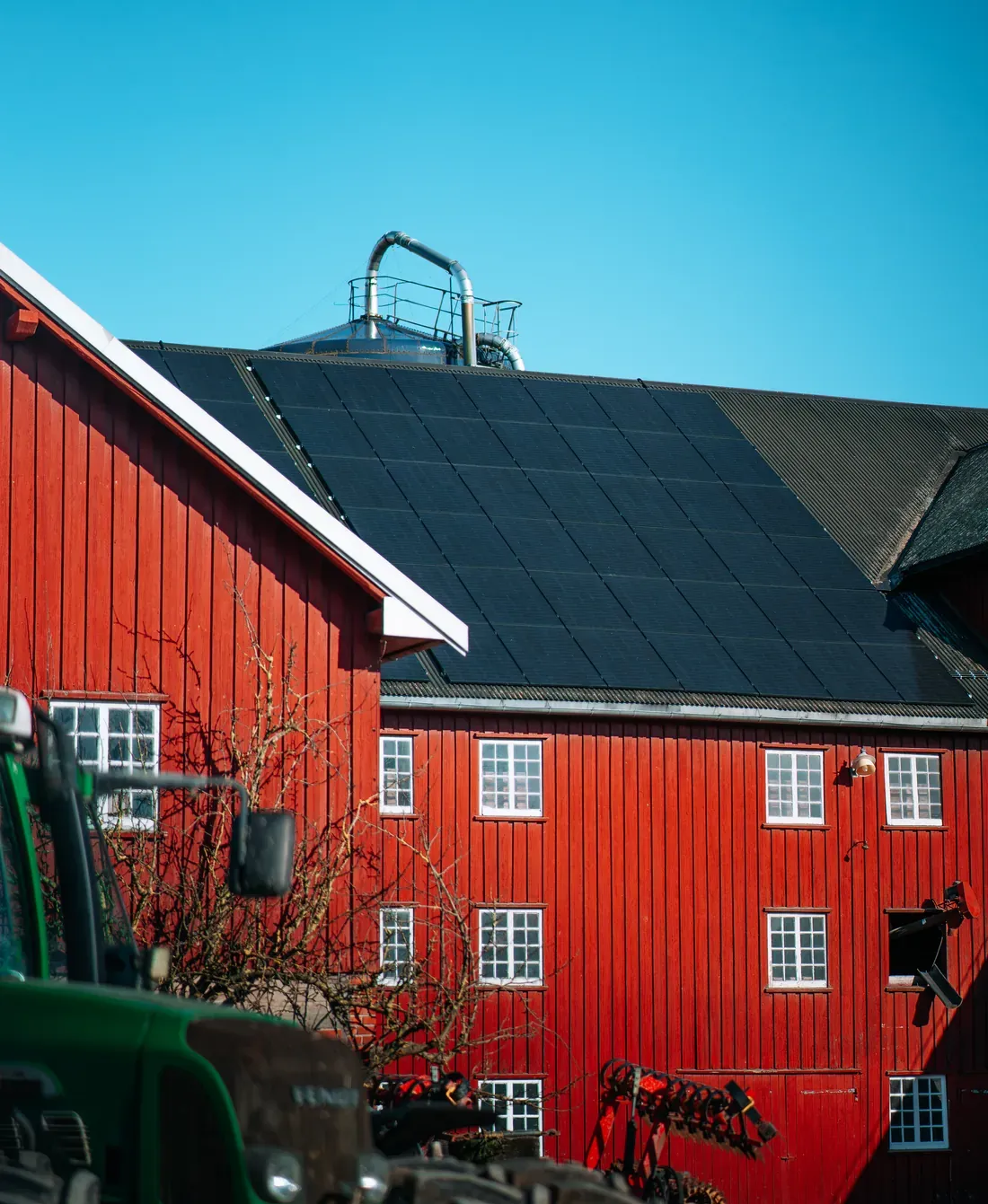 Traktor foran en rød låve med solcellepaneler på taket.